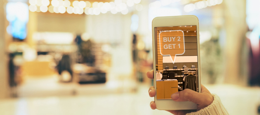 A hand holding a smartphone with a blurred background. The smartphone displays promotional items in augmented reality.